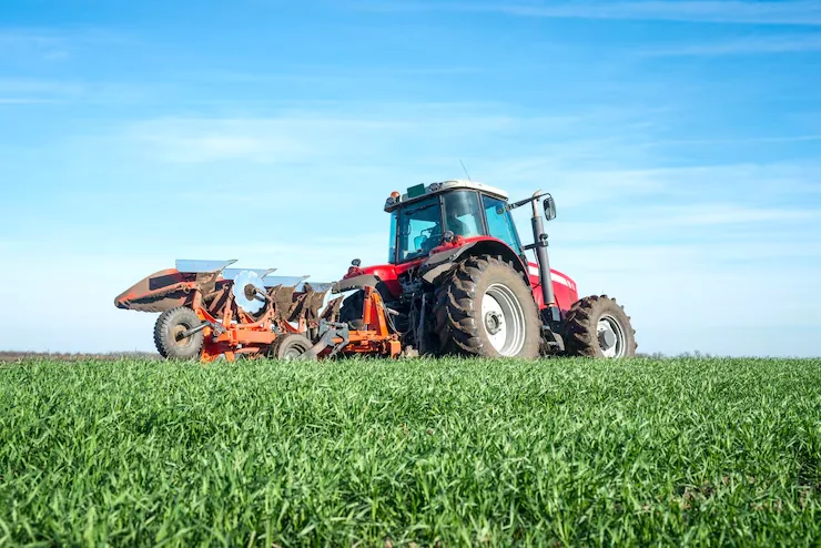 Red tractor ploughing a green field